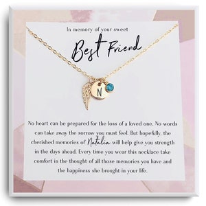 Könnte beinhalten: Eine goldfarbene Halskette mit einem Anhänger, der einen Flügel-Charm, einen runden Charm mit dem Buchstaben "N" und einen kleinen blauen Edelstein enthält. Die Halskette wird auf einer Karte mit dem Text "In memory of your sweet Best Friend" präsentiert.