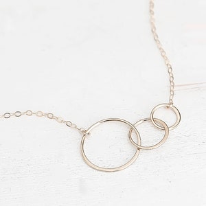 May include: A gold necklace with three interlocking circles. The circles are different sizes and are connected to a delicate chain.