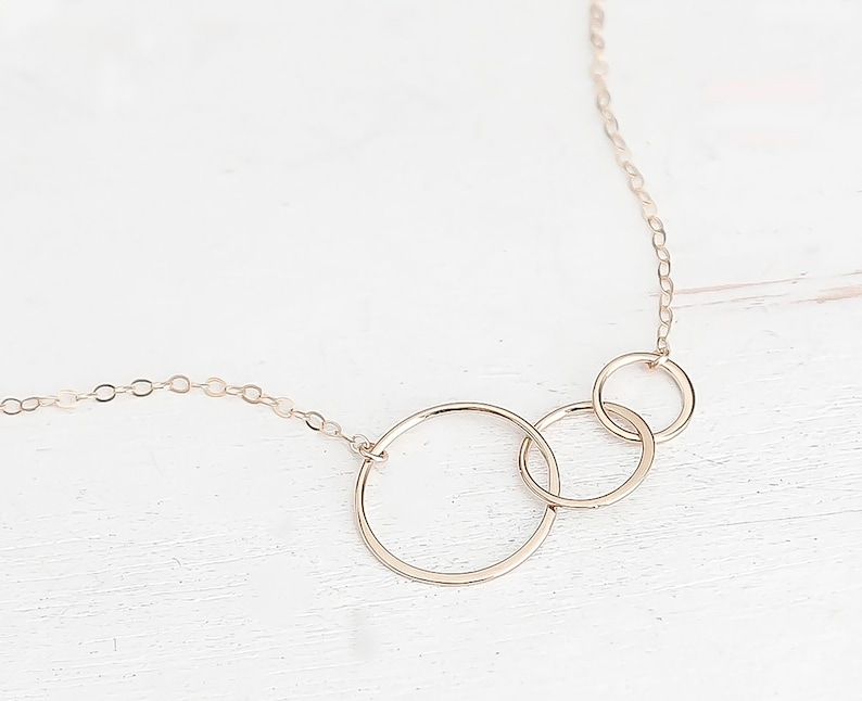 May include: A gold necklace with three interlocking circles. The circles are different sizes and are connected to a delicate chain.