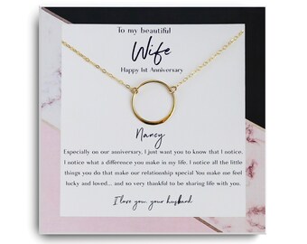 May include: A card with a pink and black marble pattern background. The card has a gold necklace with a circle pendant. The card reads "To my beautiful Wife Happy 1st Anniversary" and "Nancy". The card also includes the text "Especially on our anniversary, I just want you to know that I notice. I notice what a difference you make in my life. I notice all the little things you do that make our relationship special You make me feel lucky and loved... and so very thankful to be sharing life with you. I love you. your husband"