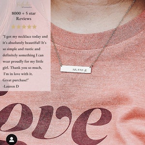 May include: A silver necklace with a bar pendant that says "mama" on a pink shirt. The necklace is on a person's chest. The shirt has the word "love" printed on it in a large font.