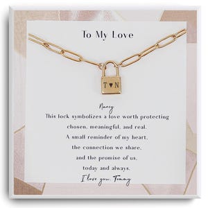 Puede incluir: Un collar dorado con un colgante de candado. El candado tiene las iniciales "T♥N". El collar se muestra en una tarjeta blanca con el texto "To My Love" y un mensaje romántico.