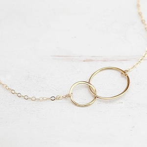 Puede incluir: Un collar de cadena de oro con dos c&iacute;rculos entrelazados como colgante.