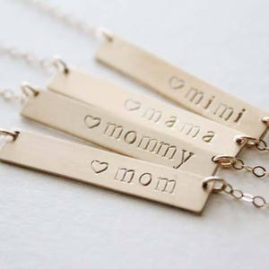 May include: Four gold bar necklaces with the words "mom", "mommy", "mama", and "mini" engraved on them. Each bar has a small heart symbol before the word.
