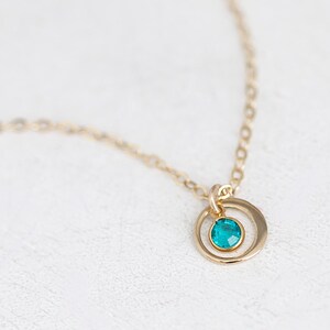 May include: A gold chain necklace with a small circle pendant featuring a teal blue gemstone.
