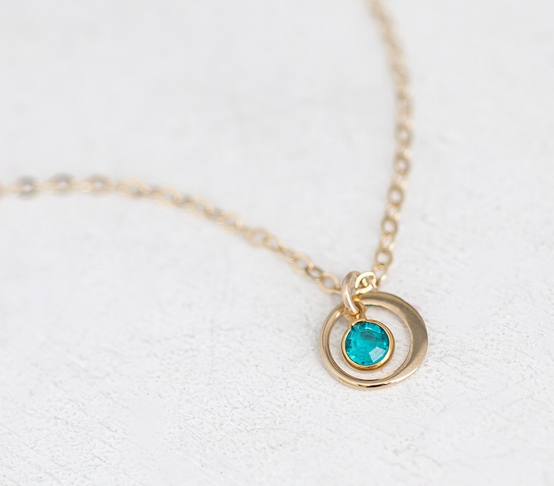 May include: A gold chain necklace with a small circle pendant featuring a teal blue gemstone.