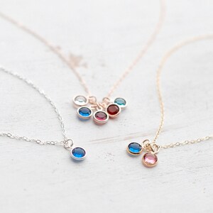 May include: Three delicate necklaces with small gemstone charms. The necklaces are silver, gold, and rose gold. The charms are blue, red, and pink.