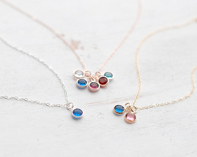 May include: Three delicate necklaces with small gemstone charms. The necklaces are silver, gold, and rose gold. The charms are blue, red, and pink.