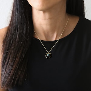 Puede incluir: Un collar de cadena dorada con un peque&ntilde;o colgante redondo de piedra preciosa azul verdoso que cuelga de un fino c&iacute;rculo dorado.