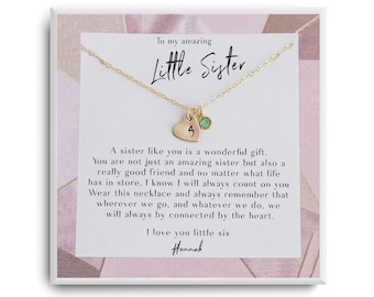 Puede incluir: Un collar de oro con un dije en forma de corazón y una pequeña piedra preciosa verde. El collar viene en una caja blanca con un fondo estampado en rosa y blanco. La caja incluye un mensaje que dice "Para mi increíble hermana pequeña" y un mensaje sincero sobre el vínculo entre hermanas.