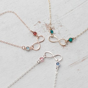 May include: Three gold infinity symbol necklaces with different colored gemstones. The necklaces feature a small, round gemstone in each of the following colors: red, blue, and green.