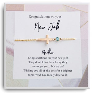 Op de afbeelding: Een witte kaart met een gouden armband met een kruisbedel en een boodschap die luidt: "Gefeliciteerd met je nieuwe baan Martha Gefeliciteerd met je nieuwe baan! Ze weten niet hoe gelukkig ze zijn om je te hebben... maar wij wel! We wensen je het allerbeste voor een stralendere toekomst! Je verdient het!"