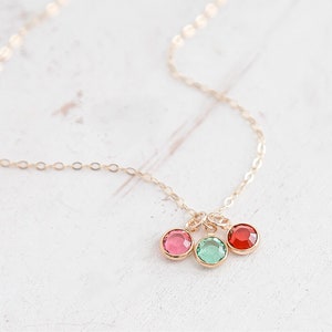 May include: A gold chain necklace with three dangling charms. The charms are round and feature red, green, and pink crystals.