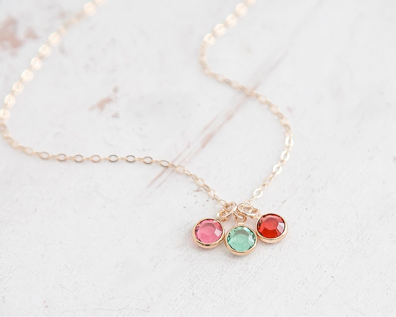 May include: A gold chain necklace with three dangling charms. The charms are round and feature red, green, and pink crystals.