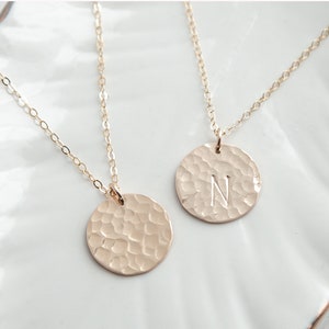 May include: Two gold necklaces with hammered disc pendants. One pendant is plain and the other has the letter "N" engraved on it.