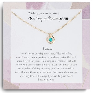 Op de afbeelding: Een gouden ketting met een turquoise edelsteenbedel en een kaart met de tekst "Wishing you an amazing First Day of Kindergarten" en "Here's to an exciting new year, filled with fun, new friends, new experiences, and memories that will shine bright for years. Learning is a treasure that will follow you everywhere. Believe in yourself because you are capable of doing anything you set your mind to. Wear this necklace as a reminder that even when we are apart my love will always be close to your heart. Love you, Nina."