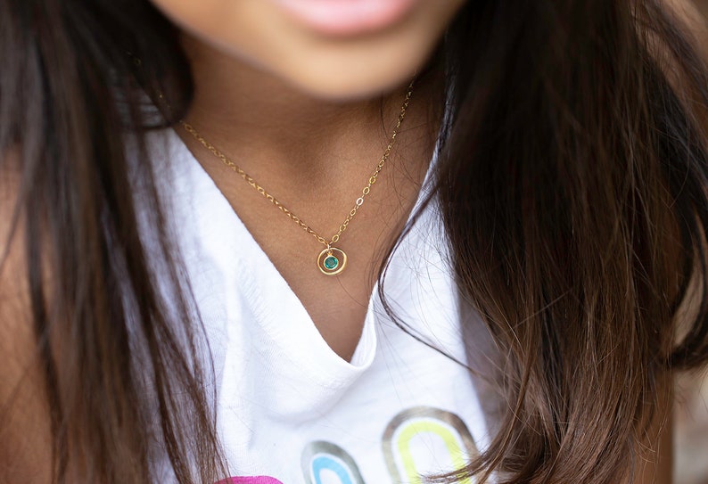 May include: A gold chain necklace with a small, round pendant featuring a green gemstone.