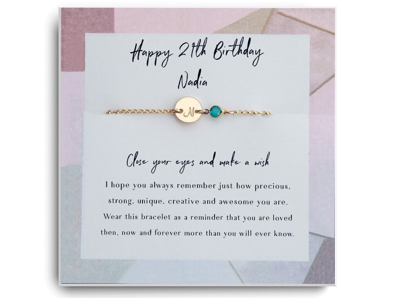 Peut inclure: Une carte avec un bracelet en cha&icirc;ne dor&eacute;e avec un petit charme en or et une perle turquoise. La carte porte le texte "Joyeux 27e anniversaire Nadia" et un message sur le fait de faire un v&oelig;u et de se souvenir de la personne pr&eacute;cieuse, forte, unique, cr&eacute;ative et formidable qu'est le destinataire. La carte indique "Portez ce bracelet comme un rappel que vous &ecirc;tes aim&eacute;(e) alors, maintenant et pour toujours plus que vous ne le saurez jamais."