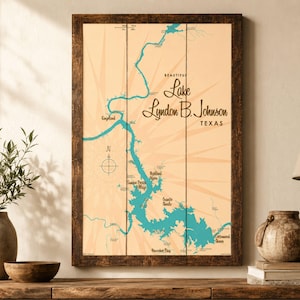 May include: A rectangular wall art piece featuring a map of Lake Lyndon B. Johnson, Texas, printed on vertical wooden planks. The map displays teal water against a light tan background with sunburst lines, a compass rose, and black text.