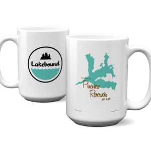 May include: Two white ceramic mugs. One mug features a black and teal "Lakebound" logo with trees and water. The other mug displays a teal map of Pineview Reservoir, Utah, with the text "Beautiful Pineview Reservoir UTAH".