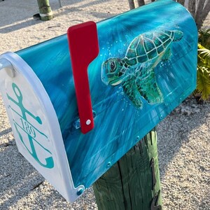 May include: A blue mailbox with a painted sea turtle design and a red flag. The mailbox has a white anchor with the number 189 on it.