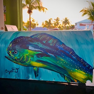 May include: A vibrant painting of a mahi-mahi fish in shades of blue, green, and yellow. The artwork features the fish swimming in a turquoise sea, with the artist's signature "crystal" in the lower left corner. The background shows a tropical scene.