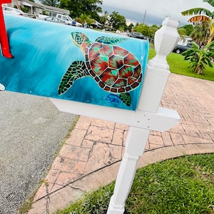 May include: A blue mailbox with a painted sea turtle design. The turtle has a green shell with red and orange accents. The mailbox is mounted on a white post.