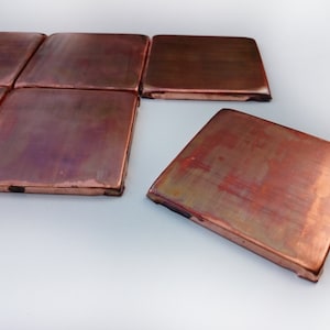Op de afbeelding: Een set koperen tegels met een geborstelde afwerking. De tegels zijn in een verspringend patroon gerangschikt en hebben een warme, metallic kleur.