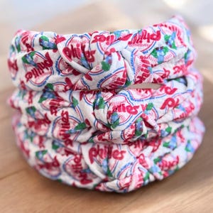 May include: Three white fabric headbands with a red and blue pattern featuring the word "Phillies" repeated throughout.