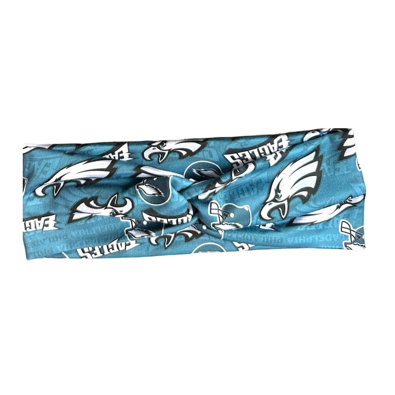 May include: A blue and white headband with a repeated pattern of the Philadelphia Eagles logo. The logo features a white eagle with a black beak and black eyes, and the word "Eagles" in black letters.