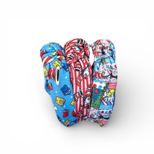 May include: Three fabric headbands with colorful patterns. One is blue with books, another is red and white striped, and the third is a patchwork design with cartoon characters. These headbands are likely for children or adults.