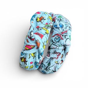 May include: A light blue knotted headband featuring colorful illustrations of characters and objects. The headband is made of a soft fabric and is designed for comfort and style. The design includes red, yellow, and green accents.