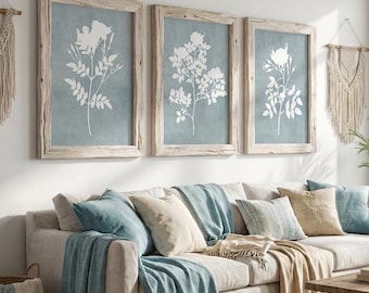 May include: A living room scene with a neutral-toned sofa, adorned with blue and beige pillows and throws. Three framed botanical prints hang above the sofa. A wooden coffee table and a woven rug complete the cozy, coastal-inspired decor. The text "IYI ART STUDIO" is visible.