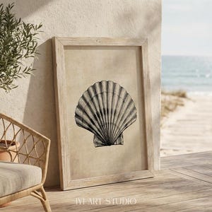 May include: A framed wall art print featuring a detailed black and white illustration of a single scallop shell centred on a textured beige background. The rectangular wooden frame has a light natural finish and holds the artwork upright.