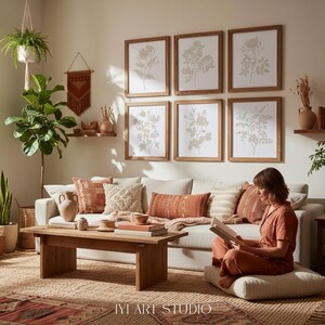 May include: A living room featuring a light-colored sofa with terracotta and cream pillows, a wooden coffee table, and six framed botanical prints on the wall. A person sits on a floor cushion reading a book. The text IYI ART STUDIO is visible.