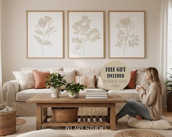 May include: Three framed wall art prints featuring beige botanical illustrations of flowers and leaves on a white background, displayed above a beige sofa with orange and patterned throw pillows, a wooden coffee table, and a round text overlay.