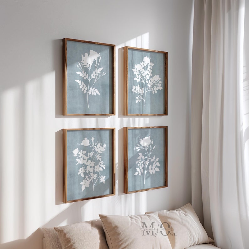 May include: Four rectangular wall art pieces in wooden frames, each featuring a white botanical illustration of flowers and leaves set against a solid, muted blue background. The prints are arranged in a two-by-two grid on a plain white wall.
