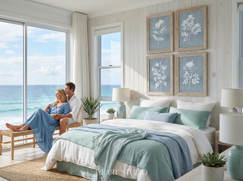 May include: A bedroom featuring a bed with white and light blue bedding, two light blue table lamps, and four framed botanical prints on a white paneled wall. A wooden bench sits near a large window overlooking the ocean.