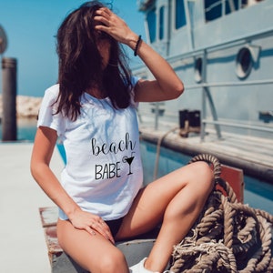May include: A white t-shirt with the text "beach babe" and a cocktail glass graphic printed on the front.