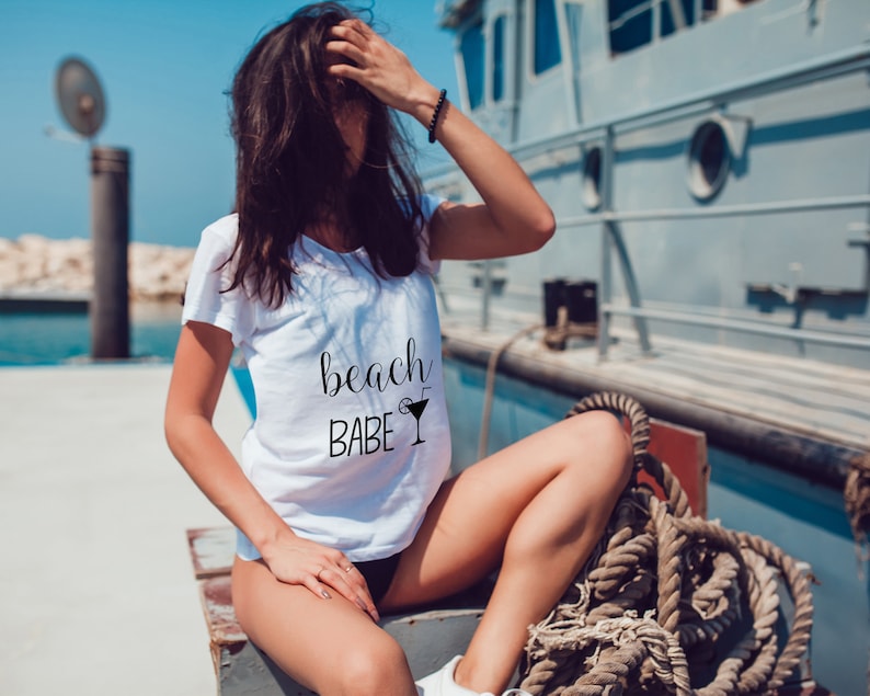 May include: A white t-shirt with the text "beach babe" and a cocktail glass graphic printed on the front.