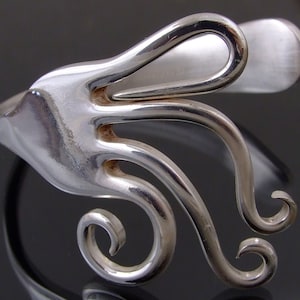 May include: A silver bracelet made from a repurposed fork, with the tines bent into a swirling design.