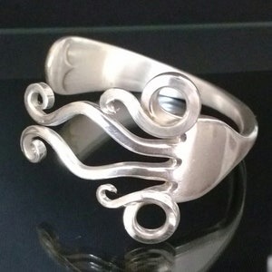 May include: Silver bracelet made from a repurposed fork, with the tines bent into a swirling octopus design.