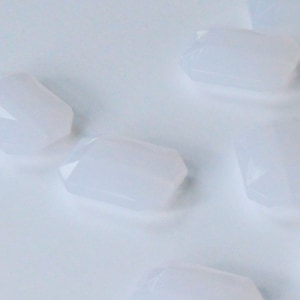 May include: A group of six opaque white, faceted, geometric shapes, resembling gemstones, are scattered on a white surface.