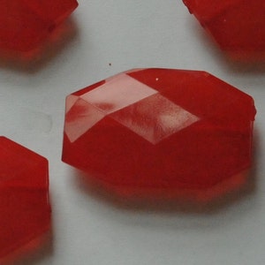 May include: A group of four red faceted glass beads. The beads are all the same size and shape, and they are arranged in a random pattern.