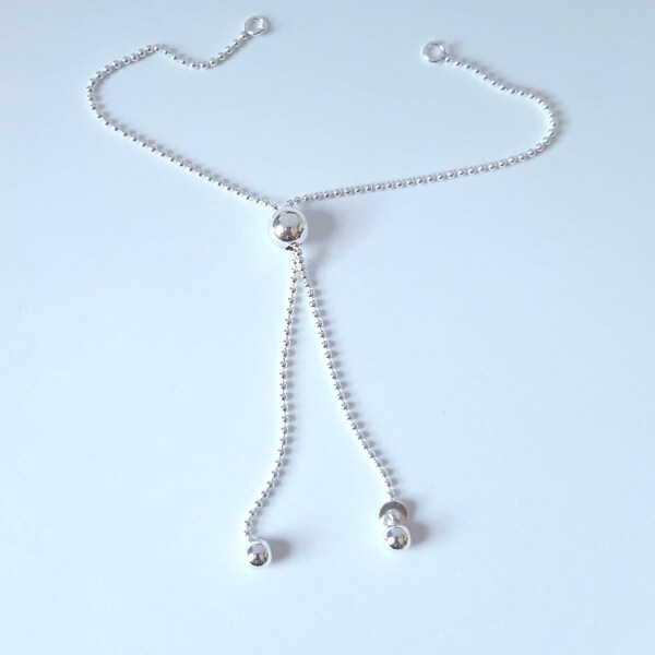 May include: A silver adjustable bracelet with a beaded chain and a round charm at the end.
