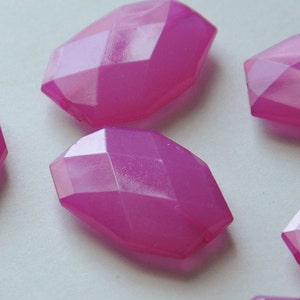 May include: A group of six pink faceted glass beads. The beads are all the same size and shape, and they have a slightly iridescent finish.