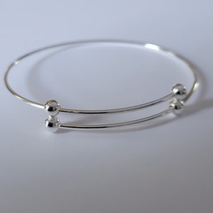 May include: A silver bangle bracelet with two rows and two small round beads at the opening.