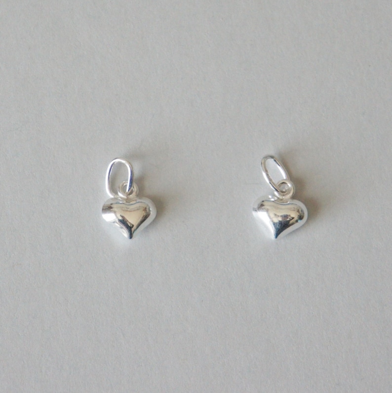 May include: Two silver heart-shaped charms with a loop at the top for attaching to a necklace or bracelet.