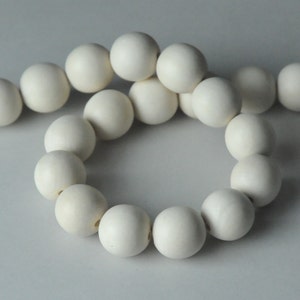 Könnte beinhalten: Eine Schnur aus weißen Holzperlen, die zu einem Kreis geformt sind. Die Perlen sind glatt und rund und alle gleich groß.