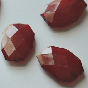 May include: Four red faceted glass beads, each with a unique shape and a slightly different shade of red.